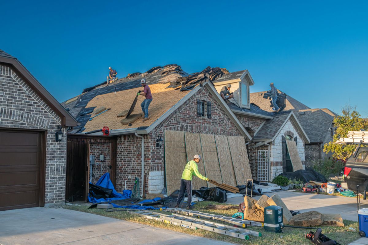 Roofing crew removing old shingles and preparing a residential home for a full roof replacement.