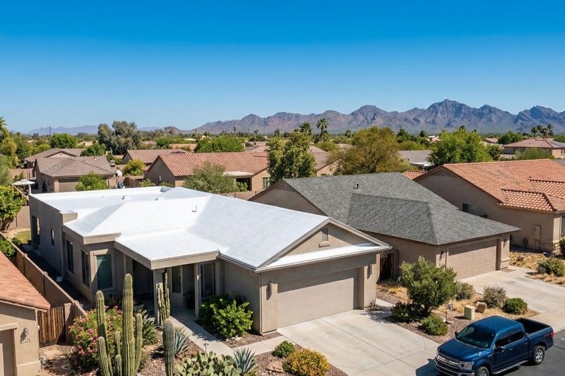 Aerial view of an Arizona home comparing a white spray foam reflective roof coating to traditional dark asphalt shingles under intense Phoenix sun.