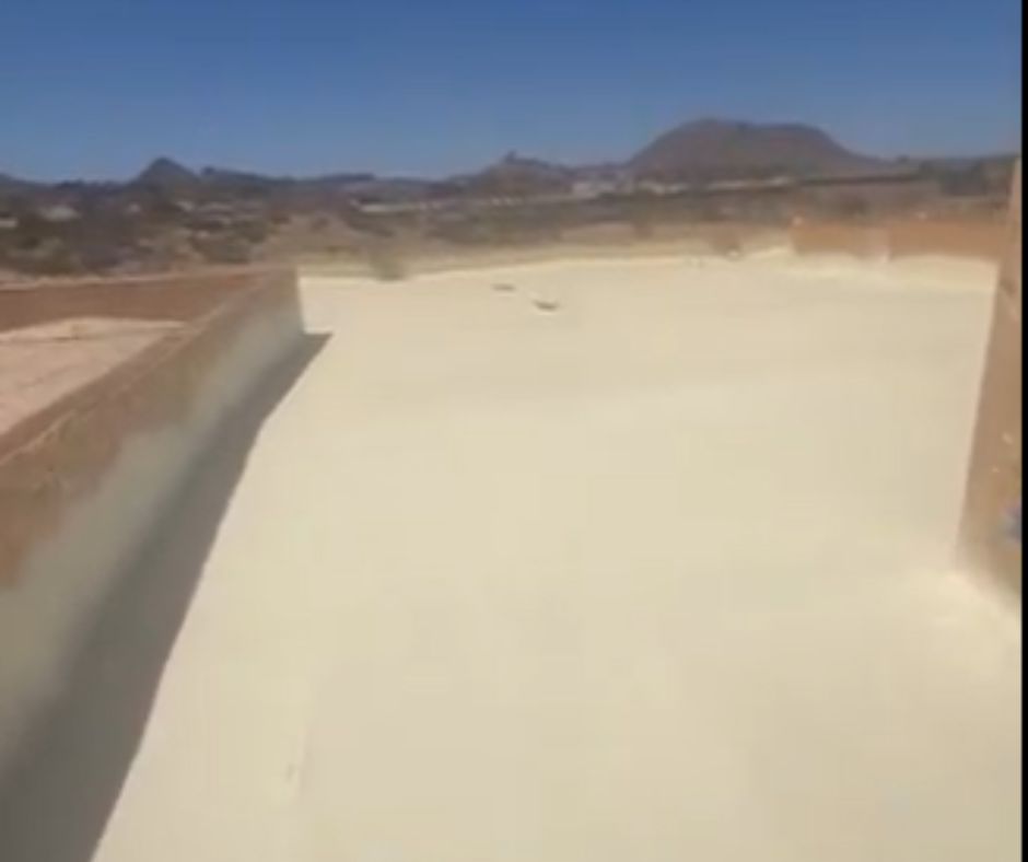 Flat commercial roof with fresh spray polyurethane foam coating, surrounded by parapet walls, with Arizona mountains in the background under a clear blue sky.
