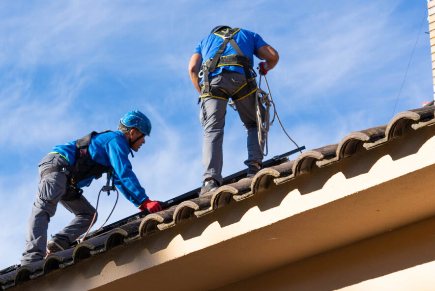 Roofing professionals inspecting and installing solar panels on a residential roof in Phoenix under clear blue skies.
