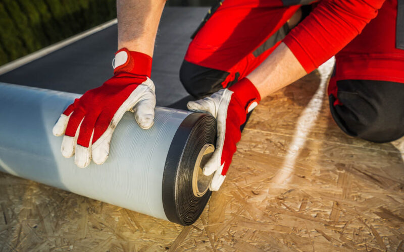 Caucasian Roofing Worker Preparing a Roll of EPDM Roof Membrane Material. Construction Industry Theme.