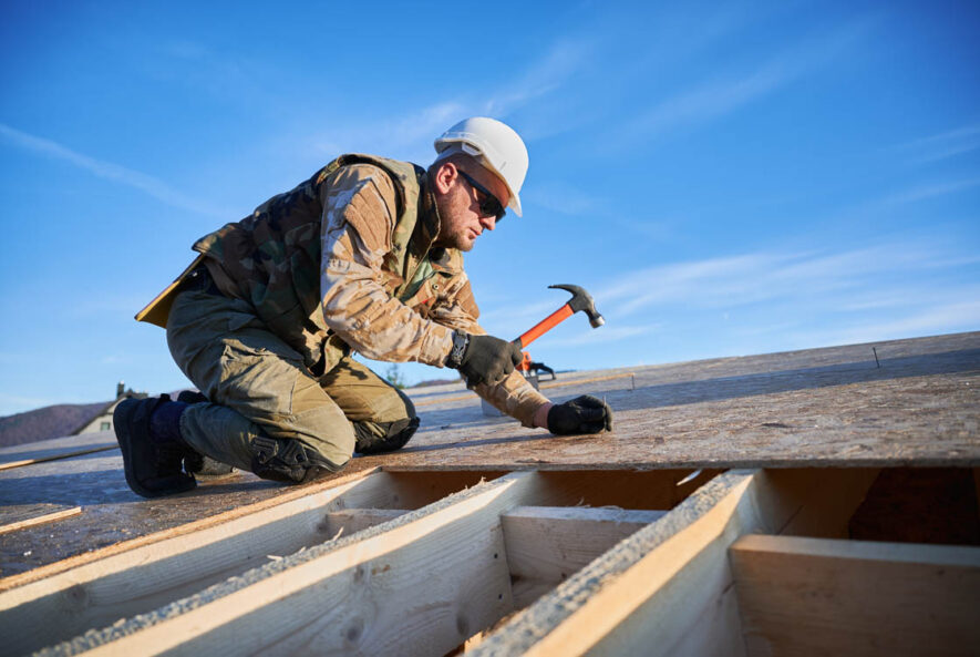 Roofer in hard hat and gloves using a hammer on wooden roofing materials, emphasizing roofing services and carpentry work by The Arizona Roofer.